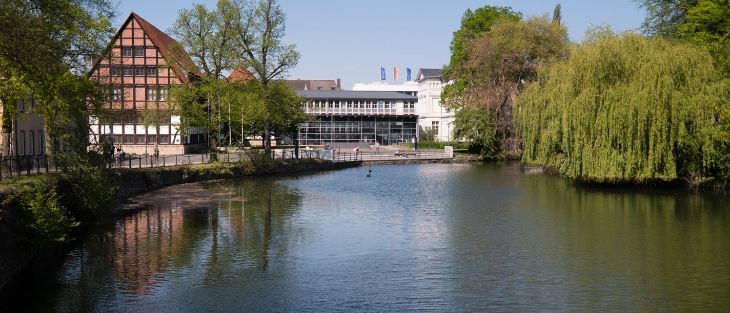 Eine ruhige Flusslandschaft mit reflektierendem Wasser; im Hintergrund das Lippische Landesmuseum.