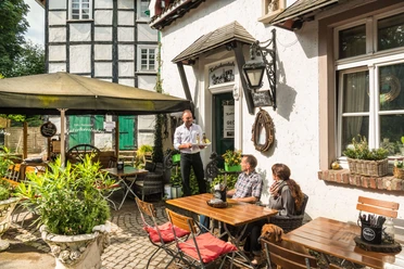 Erfrischung im Biergarten der Kutscherstuben in Wülfrath-Düssel Ein Gastro-Mitarbeiter serviert im sonnigen Biergarten zwei Gästen auf einer Terrasse Getränke.