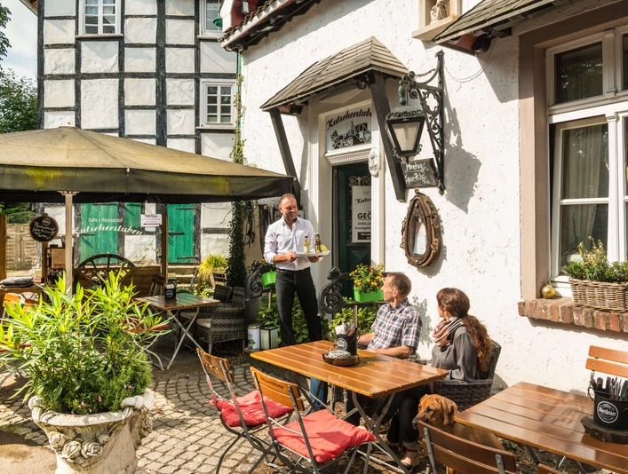 Erfrischung im Biergarten der Kutscherstuben in Wülfrath-Düssel Ein Gastro-Mitarbeiter serviert im sonnigen Biergarten zwei Gästen auf einer Terrasse Getränke.