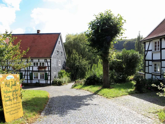 Einladender Hofladen auf dem Biohof Judt im Windrather Tal Ein Hofladen umgeben von Fachwerkhäusern und grünen Bäumen lädt im Windrather Tal zum Einkauf ein.