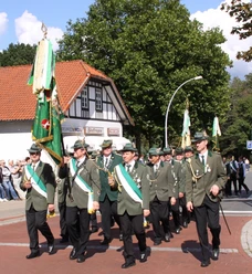 Schützenfest in Hützel Männer in grünen Uniformen marschieren mit Vereinsfahne beim Schützenfest auf der Straße.