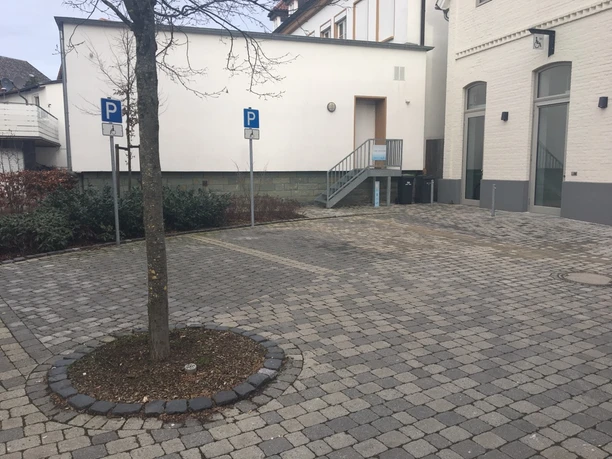 Zwei Parkplätze für Menschen mit Behinderung auf gepflastertem Hof, mit Zugang zu einem Gebäude.