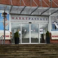 Eingang Markpassage Eingang zur Markpassage mit Glastüren, flankiert von zwei Pflanzkübeln auf einer steinernen Treppe.
