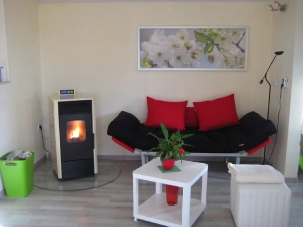 Ein Pelletofen erwärmt einen modernen Raum mit roten Akzenten, stilvollem Sofa und Zimmerpflanze.