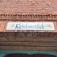 Kleinkunstdiele Bücken Das Bild zeigt das Schild der Kleinkunstdiele, aufgehängt an einer Backsteinwand mit Holzbalken.