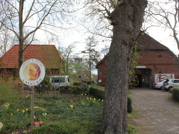 Historische Backsteingebäude mit frühlingshaften Blumen; Café-Schild rechts neben einem Baum.