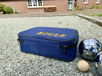 image00004.jpeg Eine Boule-Tasche aus blauem Stoff mit der Aufschrift "BOULE" und drei glänzenden Metallkugeln auf Kies.