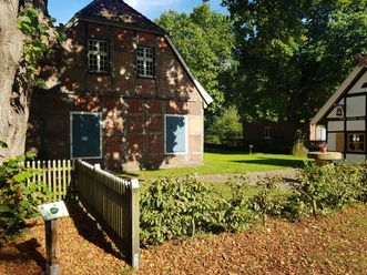 Naturspazierweg_Schapen_©SG-Spelle.jpg Backsteinhaus und Fachwerkgebäude an einem schattigen Weg im Grünen mit Bäumen und Sonnenlicht