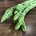Frische grüne Spargelstangen liegen gebündelt auf einer hölzernen Arbeitsfläche bereit zum Kochen.
