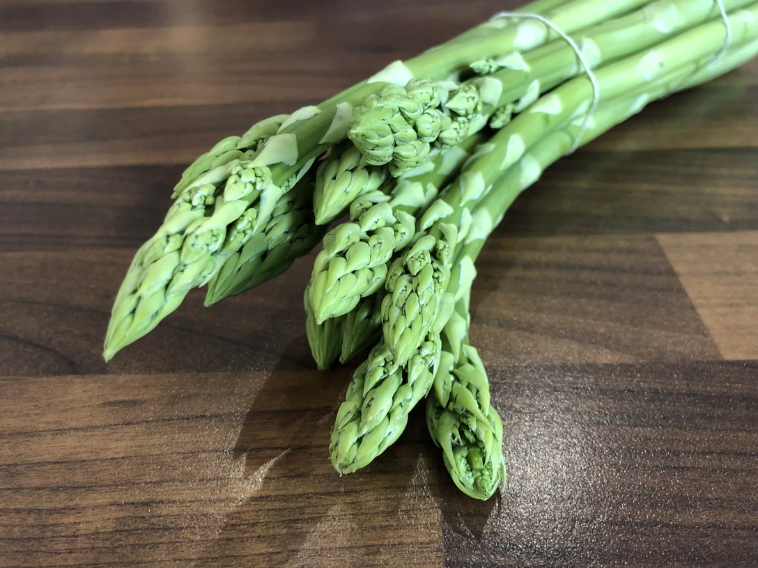 Spargel Frische grüne Spargelstangen liegen gebündelt auf einer hölzernen Arbeitsfläche bereit zum Kochen.