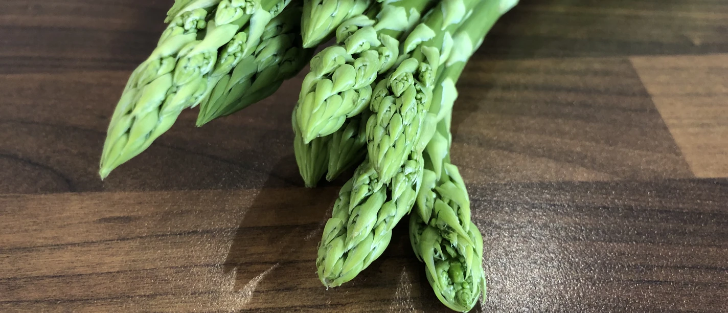 Spargel Frische grüne Spargelstangen liegen gebündelt auf einer hölzernen Arbeitsfläche bereit zum Kochen.