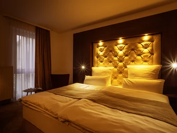 Doppelzimmer.jpg Gemütliches Hotelzimmer mit beleuchtetem, gepolstertem Kopfteil und elegantem, warmem Ambiente.