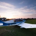 Ein kleines Flugzeug steht auf einer Grasfläche am Flugplatz Detmold, umgeben von Abendsonne.