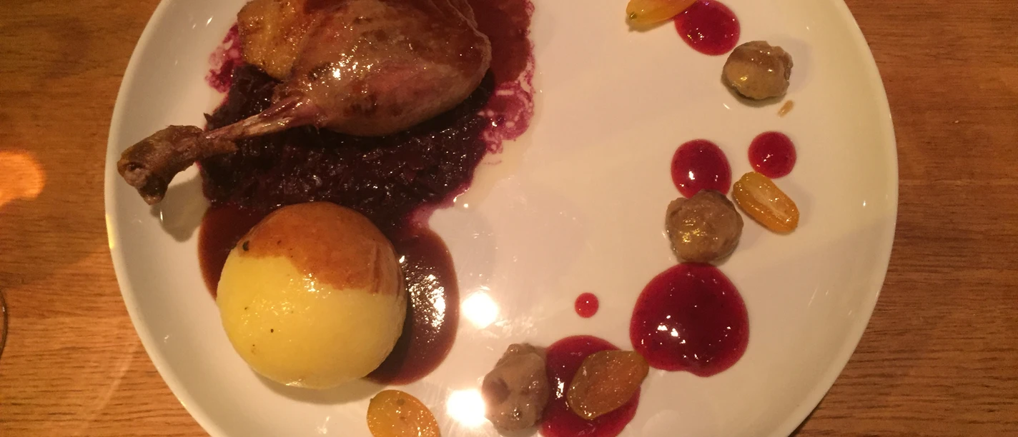 A plate of duck leg on red cabbage, accompanied by dumplings, grapes and an appealing sauce.