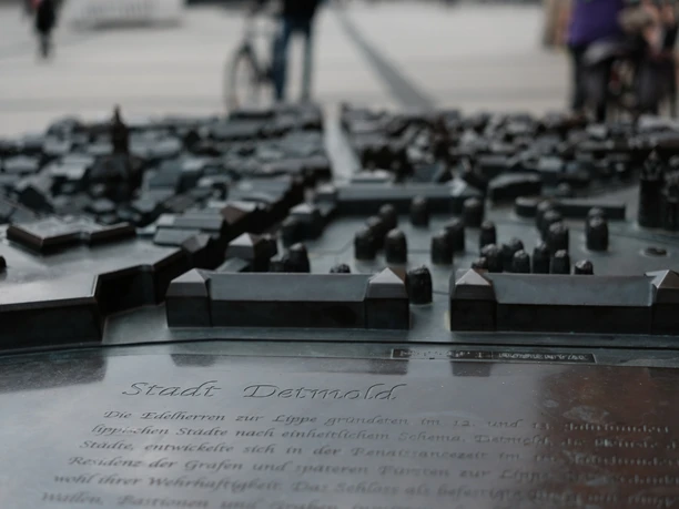 Bronzefarbenes Relief von Detmold auf einem Stadtplatz, mit erhobenen Gebäudeteilen für Tastbarkeit.