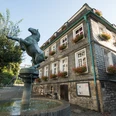 Pferdebrunnen und Stadtgeschichtshaus in Mettmann Bronzefarbene Pferdeskulptur erhebt sich über einem Wasserbrunnen vor einem Fachwerkhaus mit Blumenschmuck.