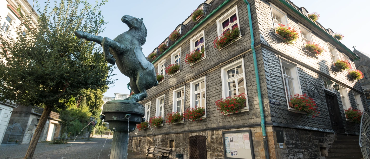 Pferdebrunnen und Stadtgeschichtshaus in Mettmann Bronzefarbene Pferdeskulptur erhebt sich über einem Wasserbrunnen vor einem Fachwerkhaus mit Blumenschmuck.