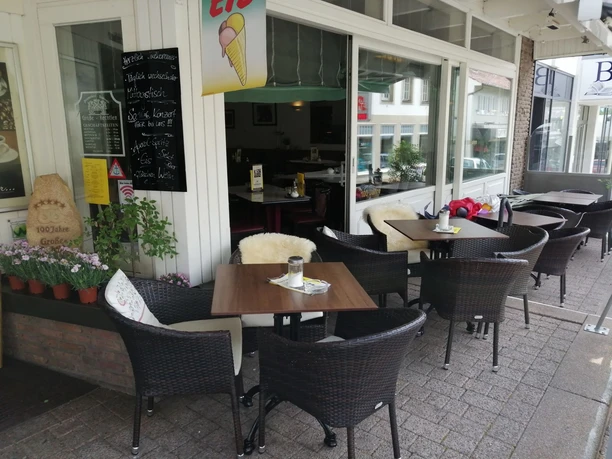 Stadtcafe_Grosse-Rechtien_Terrasse_Teutoburger Wald Tourismus_Bohlken_2000.jpg Ein gemütlicher Außenbereich eines Cafés mit Korbstühlen und Tischen in einer Fußgängerzone.