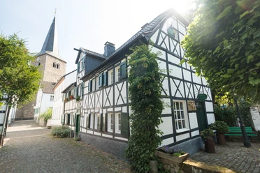 Ausflug zum historischen Stadtkern von Hilden Fachwerkhaus an gepflasterter Straße mit Kirchturm im Hintergrund. Sonniger Tag in Hilden.