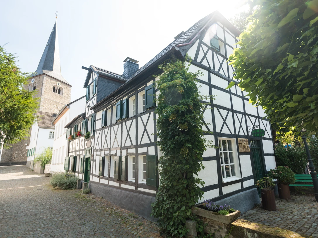 Ausflug zum historischen Stadtkern von Hilden Fachwerkhaus an gepflasterter Straße mit Kirchturm im Hintergrund. Sonniger Tag in Hilden.