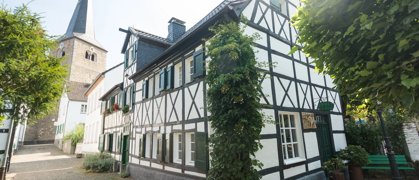 Ausflug zum historischen Stadtkern von Hilden Fachwerkhaus an gepflasterter Straße mit Kirchturm im Hintergrund. Sonniger Tag in Hilden.
