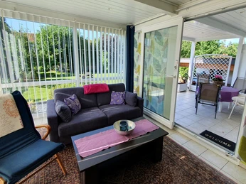 Gemütlicher Wohnbereich mit Sofas, Tisch und großen Fenstern, die auf einen grünen Garten blicken.