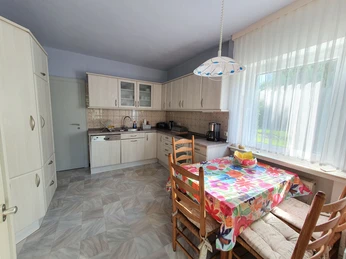 Helle Küche mit Esstisch, farbigem Tischtuch, Holzstühlen und reichlich Stauraum in Einbauschränken.