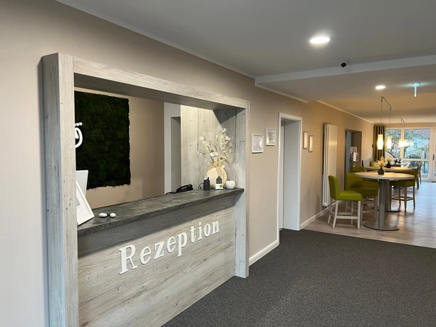 Wooden reception desk in a modern hotel with bright walls and a cozy seating area in the background.