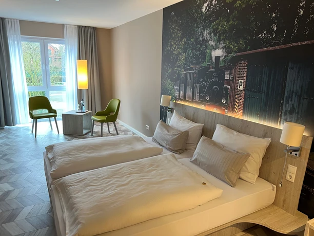 Two comfortable single beds in a modern room with a large window and mural of a historic locomotive.