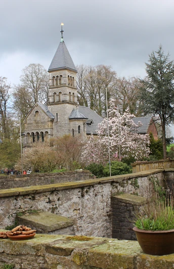 Schloss Brincke.jpg Historische Kirche mit spitzem Turm, blühende Bäume und alte Mauer in malerischer Frühlingslandschaft.