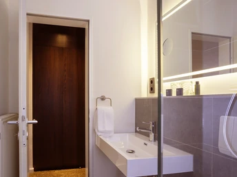 Modernes Badezimmer mit stilvoller Beleuchtung, großem Spiegel, Waschbecken und Glastrennwand zur Dusche.