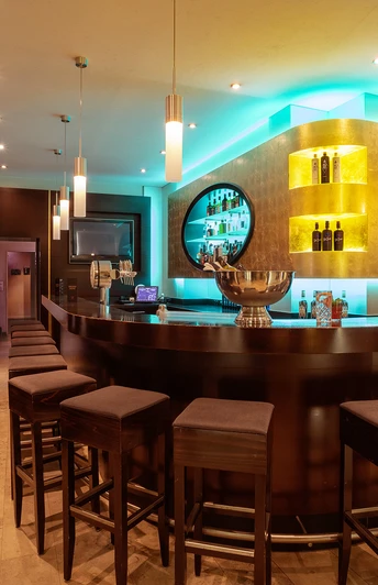 Moderne Hotelbar mit stimmungsvollem Licht, dunklen Holzverkleidungen und gepolsterten Barhockern.