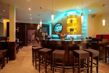 Bar.jpg Moderne Hotelbar mit stimmungsvollem Licht, dunklen Holzverkleidungen und gepolsterten Barhockern.