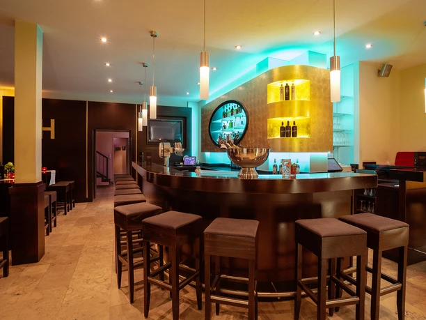 Bar.jpg Moderne Hotelbar mit stimmungsvollem Licht, dunklen Holzverkleidungen und gepolsterten Barhockern.
