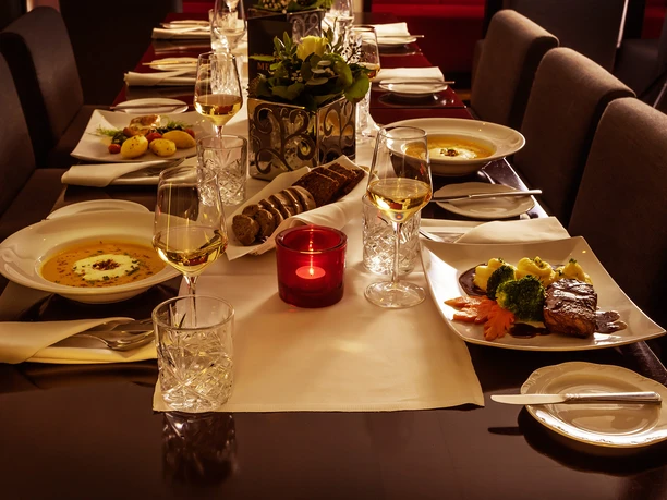 Festlich gedeckter Tisch mit elegantem Geschirr, Wein und dekorativen Kerzenlicht in stimmungsvoller Beleuchtung.