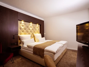 Modernes Hotelzimmer mit Doppelbett, gepolstertem Kopfteil, Teppichboden und Flachbildfernseher.