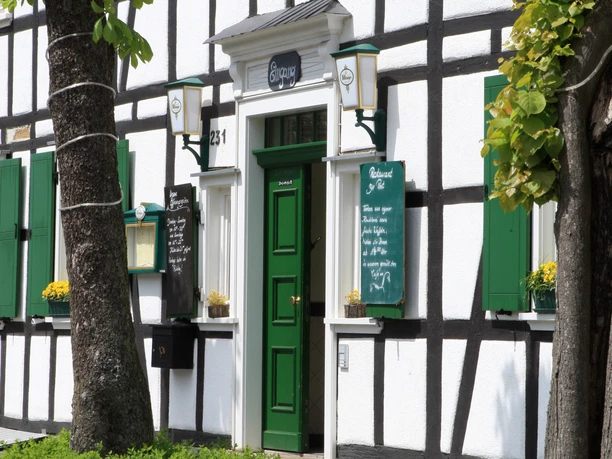 Hotel-Restaurant "Zur Post" <p>Fachwerkhaus mit grüner Tür und Schildern, umgeben von Bäumen und Blumen in Odenthal.</p>