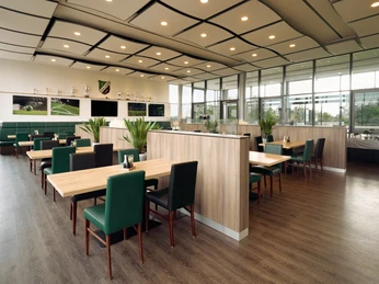 Moderne Sportslounge mit Holztischen, grünen Sitzpolstern und Trophäen an den Wänden.