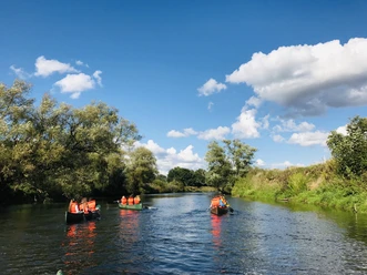 Kanu Camp Lingen.jpg Mehrere Menschen paddeln in Kanus auf einem ruhigen Fluss unter blauem Himmel mit weißen Wolken.
