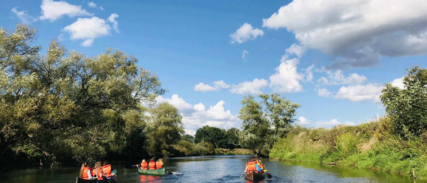 Kanu Camp Lingen.jpg Mehrere Menschen paddeln in Kanus auf einem ruhigen Fluss unter blauem Himmel mit weißen Wolken.