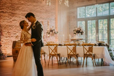 Hochzeit Ein Brautpaar tanzt in einem elegant dekorierten Raum mit festlich gedecktem Tisch im Hintergrund.