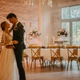 Hochzeit Ein Brautpaar tanzt in einem elegant dekorierten Raum mit festlich gedecktem Tisch im Hintergrund.