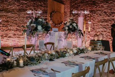 Ein festlich gedeckter Tisch in einer Scheune mit stimmungsvoller Beleuchtung und floralen Dekorationen.