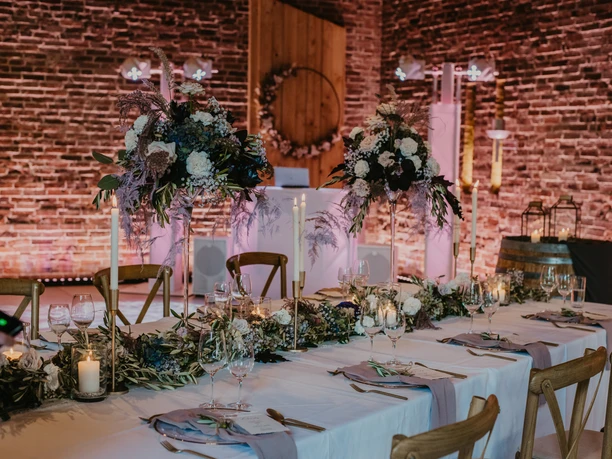 Festscheune Ein festlich gedeckter Tisch in einer Scheune mit stimmungsvoller Beleuchtung und floralen Dekorationen.