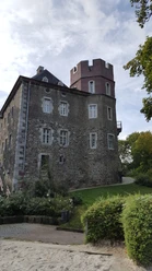 Burg Frankenberg (c)ats Steinhauer Kompaktes Bauwerk mit markanten Zinnen und aus Stein. Es liegt eingebettet in eine grüne Umgebung von Bäumen.