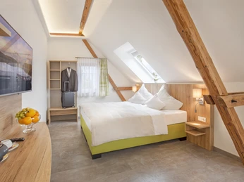 Dachzimmer im Hotel Brüngers mit Doppelbett, Holzdekor, TV, einem Obstteller und schrägem Dachfenster.