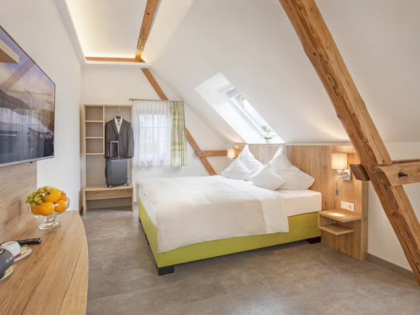 Dachzimmer im Hotel Brüngers mit Doppelbett, Holzdekor, TV, einem Obstteller und schrägem Dachfenster.