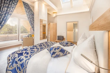 Geräumige Suite mit eleganter Einrichtung, stilvollen blauen Akzenten und Zugang zu einem Balkon.