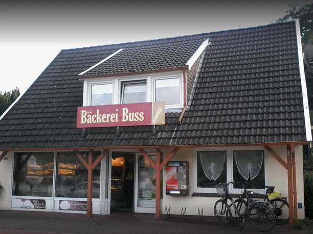 Bäckerei Buss_1.PNG Außenansicht der Bäckerei Buss mit großem Schaufenster, rotem Schriftzug und Fahrrädern davor.
