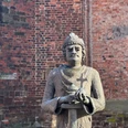 Steinfigur von Karl dem Großen vor einer Backsteinmauer, hält Kreuz und Modell einer Kirche in Händen.